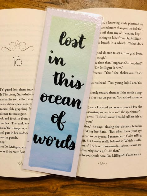 An open book lays on a table. On the book is a bookmark. The background of the bookmark is a pastel gradient of greens and blues with a thin white border. There is black text that says “lost in this ocean of words” Watercolor Bookmarks Ideas Quotes, Bookmark Painting Ideas With Quotes, Book Mark Background, Diy Bookmarks With Quotes, Gradient Drawing Ideas, Craft Bookmarks Ideas, Quotes For Book Mark, Quotes For Bookmark, Watercolor Bookmarks Quotes