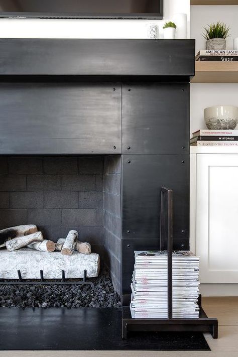 White built-in cabinets are fitted beneath stacked wooden shelves and beside a black metal fireplace boasting a black hearth and a black mantel fixed beneath a television. Black Fireplace Mantels, Black Fireplace Mantel, Industrial Fireplace, California Beach House, Industrial Chic Decor, Metal Fireplace, Black Fireplace, Regal Design, Transitional Living