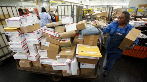 A U.S. Postal Service employee stands next to a cart full of packages. Customer Appreciation Day, Wage Gap, Futuristic Shoes, Retirement Invitations, Going Postal, Holiday Promotions, Information Age, Postal Worker, You've Got Mail