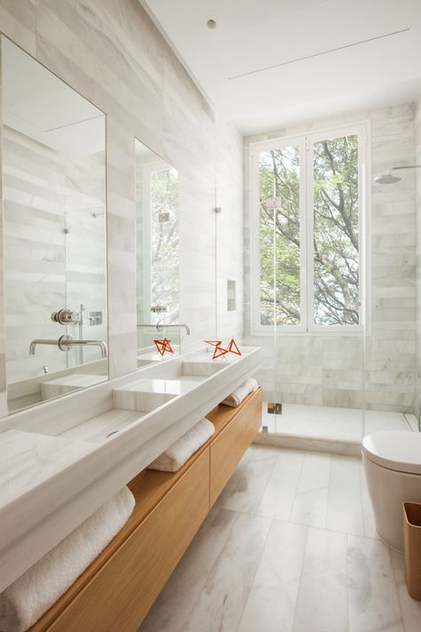 In this modern bathroom there's a wooden bathroom vanity with open shelving, that has double sinks with tall rectangular mirrors above each one. A glass shower surround allows the light from the vertical windows to pass through and fill the room, while stone tile adds a soft natural touch to the space. Wooden Bathroom Vanity, Modern Contemporary Bathroom, Contemporary Bathroom Designs, Small Remodel, Wooden Bathroom, Bathroom Windows, Trendy Bathroom, Contemporary Bathrooms, Wood Bathroom