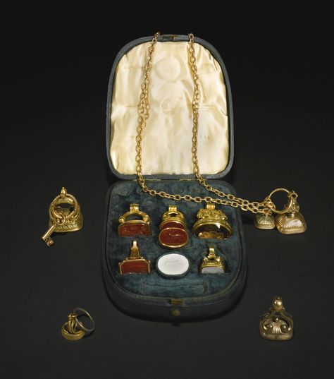 A group of ten gold and gold-cased fob seals and an intaglio ring, English, early to mid 19th century comprising a green leather case now containing five gold seals, three engraved with Crewe-Milnes arms or crest, one with a figural representation of: Le Diable emporte l'Amour, another inscribed: For / Particulars / enquire / within, and a gold ring set with an oval carnelian intaglio carved by Thamyros, signed, with a warrior standing by his horse ; a gold chain hung with two matching fob seals European Sculpture, Irish Art, European Paintings, Gold Ring Sets, Chloe Drew, Gold Case, Antique Art, Green Leather, Signet Ring