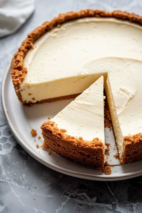 A whole cheesecake with a smooth, creamy top and a thick, crumbly crust. One slice is cut and slightly pulled out, revealing the dense, creamy interior. The cheesecake is displayed on a white plate with a marble countertop background. Friendsgiving Desserts, Healthy Pumpkin Pie Bars, Quick Thanksgiving Desserts, Friendsgiving Dessert, Desserts To Impress, Eggnog Fudge, Spice Sugar Cookies, Thanksgiving Potluck, Friendsgiving Food