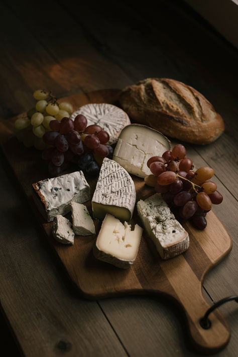 Rustic cheese board with assorted cheeses, fresh grapes, and crusty bread on a wooden table. Food On Wooden Board, Minimalist Cheese Board, Minimal Cheese Board, Rustic Cheese Board, Bread And Cheese Aesthetic, Cheese Board Photography, Charcuterie Board Photography, Cheese Platter Aesthetic, Wine And Cheese Aesthetic