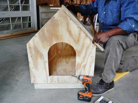 Man constructs a doghouse, while aligning roof panels on the top of the frame. Large Dog House Plans, Igloo Dog House, Dogs House, Small Dog House, Snoopy Dog House, Build A Dog House, Niche Chat, Wooden Dog House, Dog House Plans