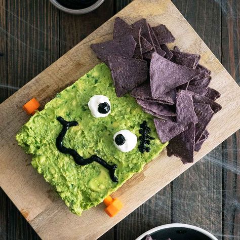 Frankenstein Guacamole is a fun idea for Halloween. Guacamole decorated with corn chips, sour cream, chipotle sauce, and carrot bolts. Frankenstein Guacamole, Halloween Burgers, Halloween Guacamole, Bacon Pickles, Theme Dinners, Blue Corn Chips, Mummy Hot Dogs, Chipotle In Adobo Sauce, Purple Corn