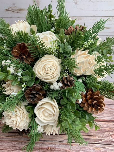 "---Wild Pine and Ivory Bouquet --- This bouquet features several types of wood roses in their natural colors of ivory along with faux pine, cedar, boxwood, baby's breath and pine cones. Flowers are handmade, which means each is unique in shape and size. Each also has variations from the wood grain and may include small flecks of bark. Flowers have beautiful and unique imperfections, as real flowers do, giving your bouquet an elegant rustic look. Custom colors are available! See our color chart Pine Bough Wedding Decor, Pine Cone Bridal Bouquet, Rustic Greenery Bouquet, Pine Tree Themed Wedding, Wedding Bouquet With Pinecones, Pine Cones Wedding Decor, Pine Color Wedding, Pine Cone Wedding Centerpieces, Cedar Bouquet