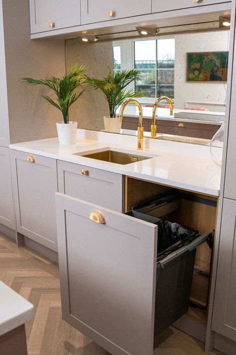 Kitchen with slim-shaker doors in a neutral cashmere tone, ornate brass gold cup handles, white worktop, brass gold quooker tap, gold sink, antique mirror splashback, pull out bin storage solution, plant, oak herringbone flooring Cashmere Kitchen White Worktop, Timber Shaker Kitchen, Cashmere And Green Kitchen, Cashmere Kitchen Shaker, Pink Shaker Kitchen, Wren Shaker Kitchen, Wren Cashmere Shaker Kitchen, Dusky Pink Kitchen, Cashmere Kitchen Colour Scheme