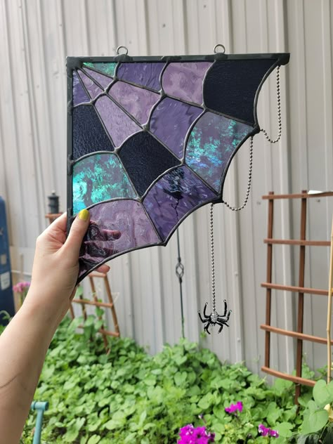 Bring an eclectic spooky vibe to your home with our purple spiderweb. This piece features a rhinestone spider (this can be omitted by request) delicately dangling from her web. Each web has a variety of purple stained glass, each boasting their own unique patterns, textures, iridescence, and opacity.  The web casts a beautiful refraction of purple light as the sun moves behind it throughout the day. Hang your web in a window corner or doorway corner, or use it as an accent piece of wall art. We love customizing with different color requests; please message us to discuss your custom color request prior to purchasing.  Overall size, specific glass used, and placement of glass may vary slightly, as each web is hand made to order. Please note photos are of previously completed designs. We stri Spider Web Stained Glass Window, Stained Glass Spiderweb, Spooky Stained Glass Art, Stained Glass Witchy, Goth Stained Glass Art, Spooky Suncatchers, Unique Stained Glass Ideas, Halloween Stained Glass Patterns, Stained Glass Halloween Patterns