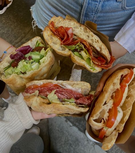 Four hands holding four different Panini with different toppings. They contain salami, tomatoes, salad, cream cheese and mozzarella. Foods In Italy, Italy Aesthetic Travel, Firenze Italy Aesthetic, Italian Food In Italy, Italy Food Aethstetic, Panini Aesthetic, Italian Food Truck, Food Moodboard, Italian Panini