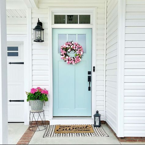 This home's white siding provides the perfect neutral background for the mint-painted craftsman style front door. A large pink tulip floral wreath is hung in the middle of the door above layered geometric and coir welcome mats. A gray wicker planter with bright pink flowers rests next to the front door. Mint Green Front Door, Craftsman Style Front Door, Transom Door, Modern Farmhouse Front Porch, Bright Front Doors, Green Front Door, White French Doors, White Front Door, Green Front Doors