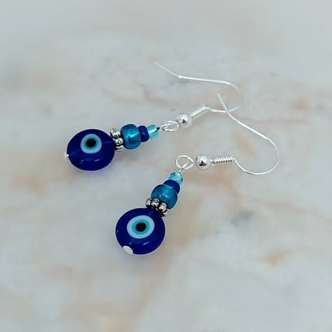 These dainty Evil Eye earrings have been lovingly made using an 8mm blue Evil Eye glass coin bead, with a Tibetan silver daisy spacer and co ordinating Preciosa and Gutermann glass seed beads above.  The Evil Eye is said to be a curse from Greek culture that has been passed through many decades and still exists today. It states that when someone is envious of you, they'll have the power to give you an 'evil glare' and send bad luck your way. In modern times, people use evil eye jewellery as a sy Evil Eye Earrings Diy, Earings Beads Ideas, Evil Eye Earring, Blue Bead Earrings, Evil Eye Crafts Diy, Evil Eye Beaded Earrings, Evil Eye Jewelry Diy, Evil Eye Jewellery, Tassel Bag Charm