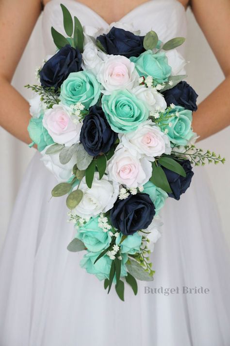 This lovely assortment of navy blue, blush pink and mint green roses is bound to turn heads on your wedding day. This lovely cascading brides’ bouquet from the is an absolutely breathtaking arrangement for any bride to be, in any season. Sage greenery and white accents complete the look and add a delicate realism to this beautiful bouquet. This bouquet is 10” wide, 18” long, and is crafted by our in-house florists without using a foam base to anchor the flowers to the bouquet. Instead, we wire o Mint Green And Blue Wedding, Teal And Mint Green Wedding, Navy And Mint Wedding, Seafoam Wedding, Navy Blue Bouquet, Turquoise Bouquet, Small Bridesmaid Bouquets, Fake Wedding Flowers, Bouquet Accessories