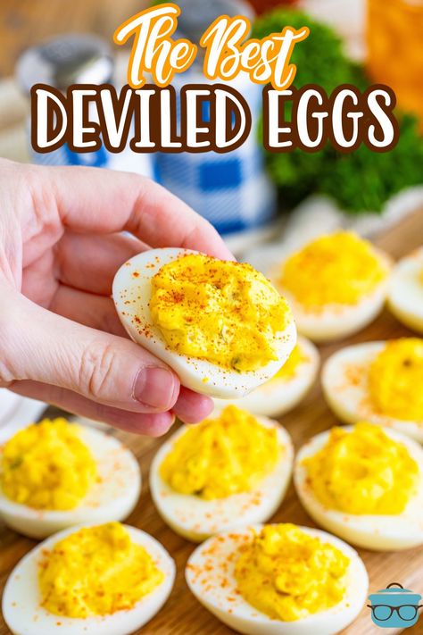 a hand holding up one deviled egg over other deviled eggs on a wooden serving board.