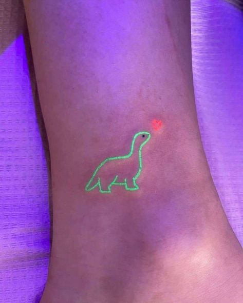 124 Glow-in-the-dark green dinosaur tattoo with an orange heart on foot under ultraviolet light. Trendy and unique body art. | Sky Rye Design Uv Tattoo Ideas, Blacklight Tattoo, Glowing Tattoos, Purple Tattoo Ink, Glow In The Dark Tattoo, Uv Ink Tattoos, Invisible Art, Glow In The Dark Butterfly, Semi Colon Tattoo