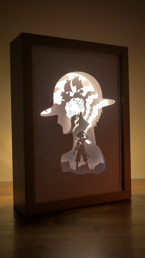 Illuminate your dark room by creating your own shadow box with this One Piece inspired Strawhat Luffy Shadow Box Shadow Box. You can DIY this easily by stacking multiple layers of paper cuts, shadow box spacers in between, a led strip light with usb switch, and a wooden shadow box frame Diorama Light Box Diy, 3d Light Box Diy, 3d Light Up Shadow Boxes, Paper Craft Frame, Shadow Box With Fairy Lights, Diy Light Box Picture Frame, Paper Light Box Diy, Shadow Light Box Diy, Anime Shadow Box Ideas