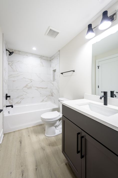 Check out this contemporary bathroom we just finished! 🛁✨ With sleek marble tiles, cool black fixtures, and warm LVP flooring. it’s the perfect blend of style and comfort.  #CustomHomeBuilder #BathroomGoals #LuxuryLiving #HomeInspo  @bobbi_lambros-designs @cat_3_photography Bathrooms With Lvp Flooring, Marble Bathroom With Black Fixtures, Lvp In Bathroom Floor, Lvp In Bathrooms, Lvp Bathroom Floor, Lvp Bathroom, Black Fixtures, Toilet Vanity, Dark Tile