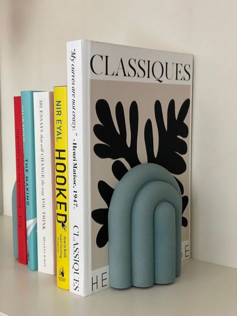 // FREE PICK UP in Toronto around Finch Station using code FREETORONTO at checkout // Elevate your bookshelf decor to a whole new level with our Nordic Elegance Bubbly Rainbow Bookend. This unique and eye-catching piece seamlessly blends minimalist design with a touch of whimsy, making it the perfect addition to your home or office. Crafted with precision and care, this bookend is a work of art that also serves a functional purpose, keeping your favourite books organized and stylishly displayed. All our products are handmade and made of natural raw concrete. Each piece may be slightly irregular and unique due to the nature of concrete, air bubbles and texture. Felt pads are applied to the bottom for scratch resistance. Comes in 2 pieces. Bookends Decor, Clay Bookends Diy, Clay Book Ends, Book Ends Aesthetic, Pottery Book Ends, Ceramic Pottery Book Ends, Clay Bookends, Air Dry Clay Bookends, Bookends Diy