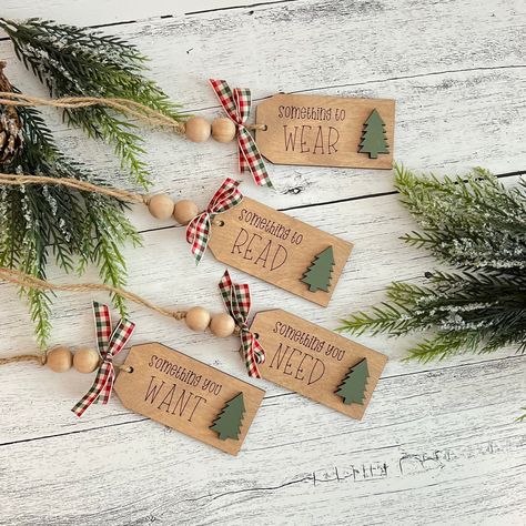 Give a gift with purpose this year with our wooden gift tags! Each set includes four tags:  1. Something To Read 2. Something To Wear 3. Something You Want 4. Something You Need Tag Dimensions: Height: 1.75 inches Length: 3.5 inches Depth: .25 inches Each tag is finished off with bead accents and a red, green and white bow!  Please Note: You are purchasing the set of four tags only. The accessories are used for staging purposes only. Christmas Wood Tags Diy, Wood Gift Tags Diy, Wooden Gift Tags Christmas, Wooden Tags Ideas Diy, Cricut Gift Tags, Gift Tags Diy Handmade, Christmas Gift Tag Ideas, Wooden Christmas Tags, Gift Tag Ornaments