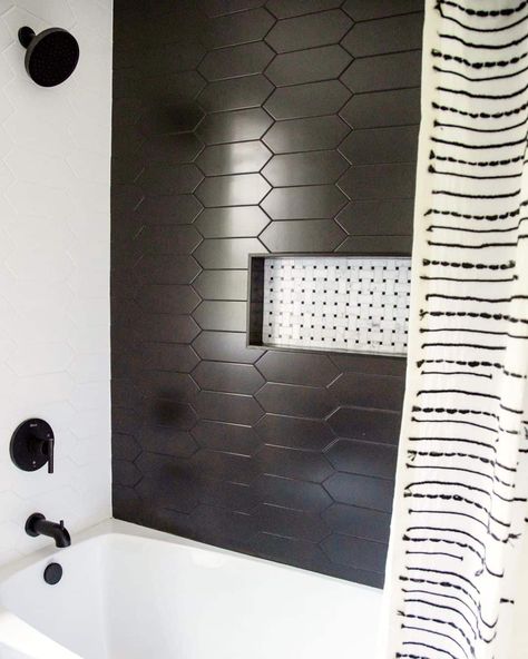 White and black tile niche with black shower niche trim is fitted into a black elongated hexagon tile shower accent wall. A white drop-in tub is fitted below the niche under a black faucet kit. Black Tile Tub Surround Ideas, Black Penny Tile Shower Wall, Black Shower Tub Combo, Black Shower Surround, Black Shower Tile With Tub, White Tub Black Tile Surround, White Shower Tile Black Grout, Black Tile White Tub, White Tub Black Tile