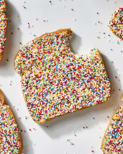 Overhead shot of a piece of fairy bread with a bite taken from the top right, on a white surface, and extra rainbow sprinkles scattered on the surface. Rainbow Savory Food, Confetti Bread, Rainbow Crispy Treats, Fairy Bread Recipe, Sprinkle Cookie Sandwich, Australian Childhood, Rainbow Bagels, Rainbow Baking, Ice Cream With Rainbow Sprinkles