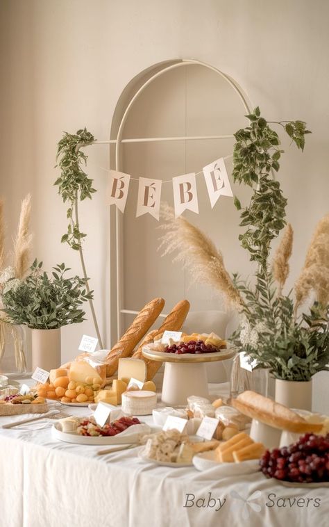 The baby shower table, a showcase of elegant baby shower ideas, is adorned with various cheeses, fruits, bread, and pastries. Greenery and pampas grass decorate the space, while a "Bébé" banner hangs above. The soft French market theme adds a graceful touch to the celebration. European Baby Shower Theme, Display Shower Ideas, Bakery Baby Shower Theme, 2025 Baby Shower Themes, Picnic Themed Baby Shower Ideas, Romantic Baby Shower Ideas, Classic Baby Shower Decor, Baby Shower Peter Rabbit Theme, French Baby Shower Ideas