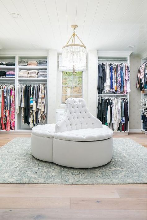 Luxurious custom closet is illuminated by a white beaded chandelier hung from a white shiplap ceiling over a white round tufted storage settee placed on a cream and blue rug covering a light gray wash wood floor. Closet Ottoman, Luxury Crib, Closet Hacks, Walking Closet, Dream Closet Design, Walk In Closet Design, White Shiplap, Dream Closets, Large Closet