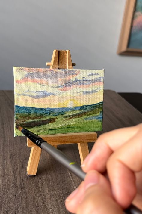 Paintbrush painting on a mini canvas and easel. Painting depicts a landscape of sunrise on middle right at the horizon line of a flower field Landscape Mini Canvas Painting, Small Acrylic Painting Mini Canvas Tutorial, Tiny Flower Painting Acrylic, Mini Acrylic Paintings, Miniature Painting Flowers, Beautiful Flower Field, Mini Easel Painting, Canvas And Easel, Mini Canvas With Easel