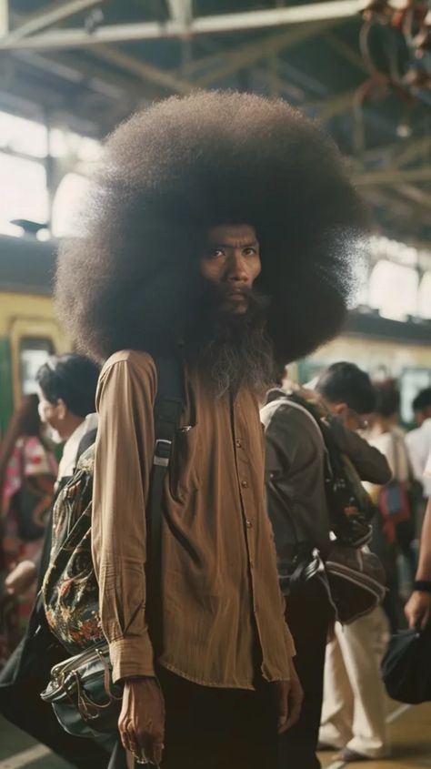 The photo shows a man with an extremely large afro. He is wearing a brown shirt and a backpack. He is standing in a busy train station, and there are people all around him. The man is looking at the camera with a serious expression. Biggest Afro In The World, Busy Train Station, Black Men Afro, Old Black Man, Large Afro, God Armor, Crowded Train, Real References, Afro Hairstyles Men