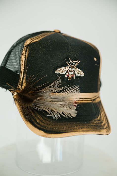 Look sharp and show off your style with this GOLDEN BEE BLACK TRUCKER HAT. This unique hat features a black trucker hat with gold accents, a gold bee patch, and a black and white feather combo that is sure to turn heads! Rock this hat and look cool and stylish - no bee-lieving required! This is a made-to-order item. All customized orders are currently shipping within 14 business days. To receive item quicker, expedited shipping is available at checkout. Bridal Trucker Hats, Trucker Patch Hats, Cool Hat Designs, Women’s Trucker Hats, Trucker Hats With Patches Diy, Diy Trucker Hat Ideas, Cute Trucker Hats, Painted Trucker Hats, Custom Hat Ideas