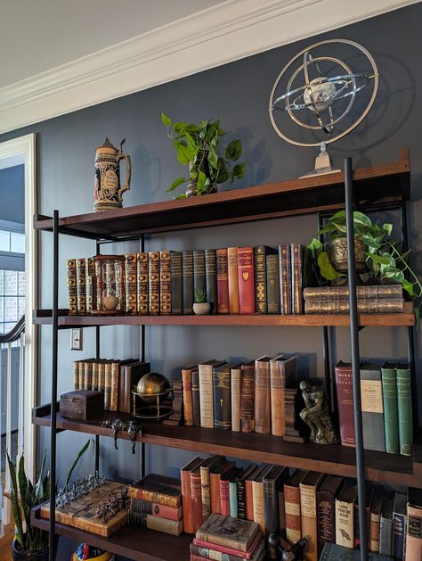 Wall color is apparently "Sherwin Williams Outerspace". Bookcase is apparently "the Beckett Storage Bookshelf from Crate and Barrel". Image originally uploaded at: https://old.reddit.com/r/AmateurRoomPorn/comments/16ju6pj/living_room_with_a_moody_whiskey_bar_vibe_in/ Moody Bookshelf, Whiskey Lounge, Living Room Shelf, Storage Bookshelf, Room Shelf, Bookcase Styling, Whiskey Bar, Book Room, Living Room Shelves