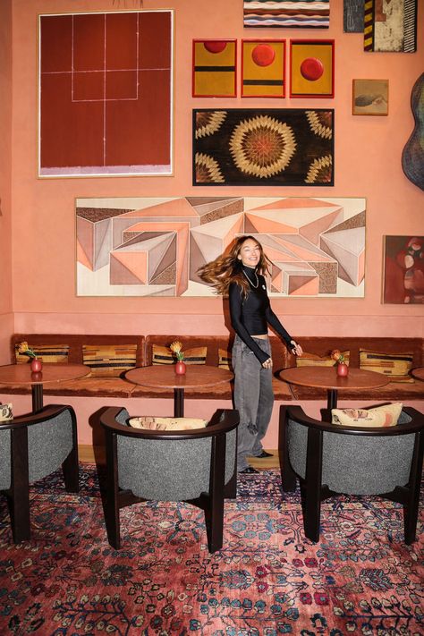 Kelly Wearstler Interiors - Restaurant Interior Design: In this image, Kelly Wearstler stands in Dahlia, the restaurant and cocktail lounge that she designed for the Downtown LA Proper Hotel. The space features vintage rugs, black idning room chairs, decorative pillows, painted walls in a pink shade and wall art. The pink wall has colorful wallpaper, colorful wall art, and abstract painting. Tap the pin to explore more of this space and for more restaurant design and restaurant aesthetic. Kelly Wearstler Wallpaper, Kelly Wearstler Interiors, Proper Hotel, Restaurant Aesthetic, Wallpaper Colorful, Cocktail Lounge, Painted Walls, Kelly Wearstler, Pink Wall