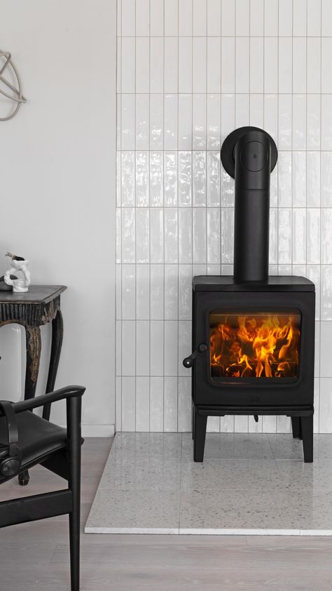 A black woodburning stove in front of a fireplace wall with white modern looking tiles and terrazzo tiles on the floor. Modern and scandinavian look. Corner Wood Stove Ideas Modern, Small Stove Fireplace Ideas, Ceramic Wood Stove, Tile Behind Wood Burning Stove, Small Indoor Fireplace, Wood Stove Tile Wall, Wood Stove Tiles, Wood Burning Stove Modern, Tile Behind Woodstove