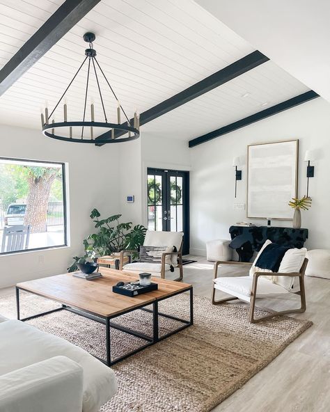 Black painted wood beams in living room are attached to a sloped white shiplap ceiling. A black wagon wheel chandelier is mounted to the ceiling above a light wood and black metal coffee table. Modern Farmhouse Living Room Ceiling Fan, Beams In Living Room, Ceiling Beams Living Room, Vaulted Ceiling Ideas, Beams Living Room, Vaulted Ceiling Living Room, White Beams, Modern Farmhouse Living, Black Living Room