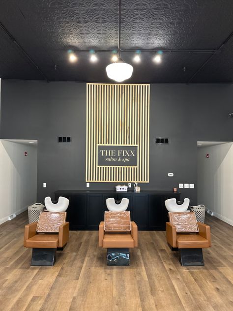 Black wall with vertical poplar wood slats, creating an accent wall. In the center, it says “THE FIXX SALON & SPA” Accent Wall For Salon Suite, Hair Salon Feature Wall, Salon With Black Walls, Salon Suite Accent Wall Ideas, Black Accent Wall Salon, Salon Picture Wall Ideas, Black And Wood Salon Decor, Black Wall Salon, Hair Salon Accent Wall