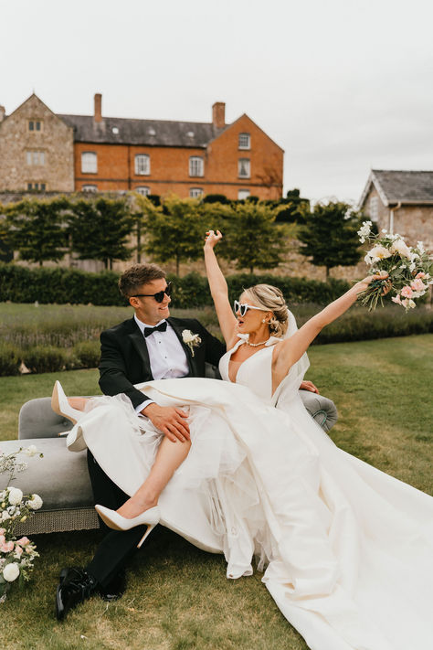 Groom in black tuxedo with black sunglasses sitting on grey sofa with the bride in a bow wedding dress with white court heels wearing white retro sunglasses | bridal style | bridal accessories | wedding sunglasses | Jessica Hopwood Photography Accessories For Bride, Wedding Sunglasses, Bow Wedding, Grey Sofa, Bow Wedding Dress, Bridal Accessories Jewelry, Court Heels, Elopement Photos, Black Tuxedo