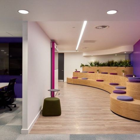 Tiered Seating Zone | Office Design and Collaboration | Morgan Lovell | These cool, curved auditorium-style benches are great for breakout meetings or for large Town Hall meetings or presentations. Colourful pink and purple cushions provide cool office branding whilst wood surfaces and planters bring a more natural feel to the space to enhance wellbeing. #Collaboration #BreakoutArea #TieredBenches #OfficeDesign #OfficeInteriorDesign Curved Office Design, Office Tiered Seating, Tiered Seating Office, Stepped Office Seating, University Lounge Design, Modular Office Seating, Best Office Design, Retractable Seating Auditorium, Lounge Room Design