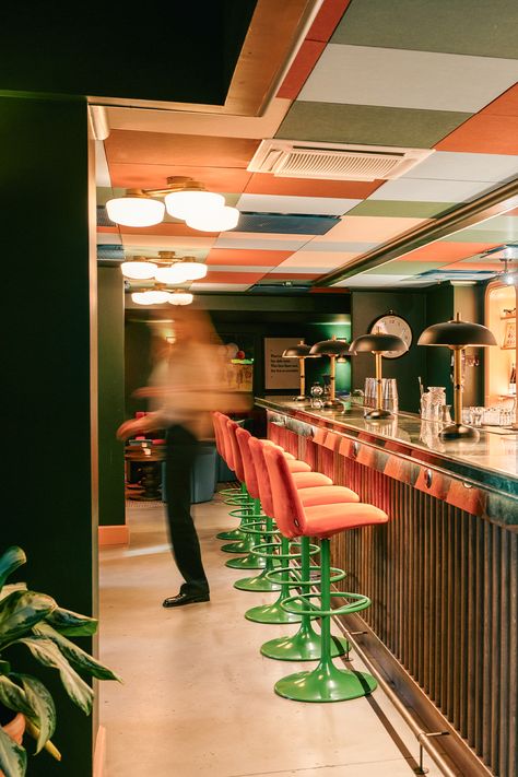 The bar area of a hotel that has a colourful checkered ceiling design and pink bar stools Ceiling Baffle Design, Corporate Ceiling Design, Restaurant Ceiling Design, Colourful Ceiling, Suspended Ceiling Tiles, Restaurant Ceiling, Office Ceiling, Bar Ceilings, Cafe Ideas