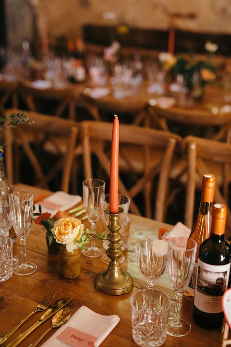 This shows a wedding dining set up. The focus is on the top of one of the tables, showing vases, glassware, brass candlestick with an orange candle, and napkins with personalised stationary. Brass Candlesticks Wedding, Brass Candle Holders Wedding, Candlestick Collection, Brass Candle Stick, Candle Sticks Wedding, Brass Candle Holder, Vintage Brass Candlesticks, Brass Candlestick, Brass Candle Holders