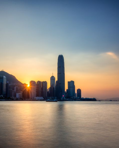 Long exposure with the sun just going down over the skyscrapers of Hong Kong Island. Showing the Two IFC as the tallest building in the Central District with a long shadow over the smooth water surface of Victoria Harbour. Hong Kong Sunset, Interesting Photos, Shanghai, Places To Travel, New York Skyline, Hong Kong, Cool Photos, China, Travel