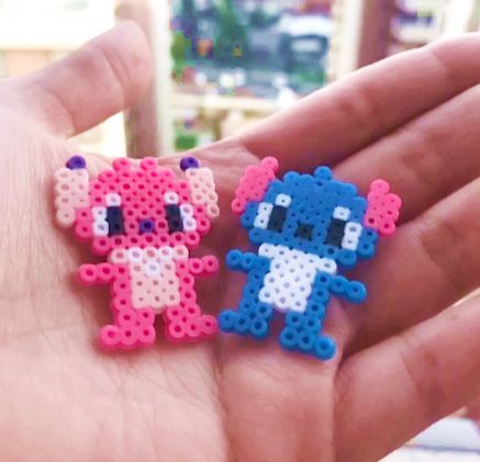 Uma mão cor de pele clara aberta, segurando dois bonecos, um da Angel(rosa e rosa claro) e um do Stitch(azul e branco) do filme Lilo & Stitch, feito de hama beads ou perler beads, que são como bolinhas, para fazer artesanato, formas, personagens, etc. Perler Beads Stitch, Hama Beads Disney, Hama Disney, Beads Stitch, Mini Hama Beads, Angel Stitch, Melty Bead Designs, Beads Perler, Melt Beads Patterns