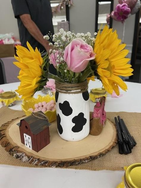 Cowgirl baby shower. Cow print mason jar with the rim rapped in twine filled with sunflowers, pink roses and baby's breath. I received so many compliments on this simple decor. Cow Mason Jar Centerpieces, Pink Western Centerpiece Ideas, Cow Print Mason Jar Centerpiece, Cow Print Centerpiece Ideas, Cow Birthday Party Centerpieces, Pink Cow Print Baby Shower Ideas Girl, Cow Print Decorations Birthday Parties, Cow Print Gender Reveal Ideas, Pink Cow Print Birthday Party