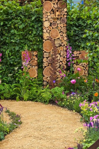 Log and wood bug hotel in Stop and Smell the Flowers by Julie Haylock. Natural Wooded Backyard Landscape, Logs In Garden, Bug Hotel Ideas, Smallholding Ideas, Wood Sculpture Ideas, Logs Ideas, Bin Store Garden, Coloured Furniture, Bug Garden