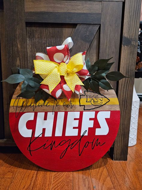 "Kansas City Chiefs Wood Door Hanger. Are you a fan of the red kingdom?! Chiefs Kingdom is where it's at! Show your red and gold pride! Are you ready for some football?!? Let all your guest know you're a fan by displaying this wood hanger all year long, during football season, or just on those special game days!  The final touches are a wired ribbon bow and greenery. RIBBONS and GREENERY may vary slightly! 14\"x14\" or 18\" x 18\" round wooden sign. Always handmade to order!" Kansas City Chiefs Craft, Chiefs Crafts, Red Kingdom, Chiefs Kingdom, Wooden Door Sign, Football Crafts, Wood Door Hanger, Wood Hanger, Door Signs Diy