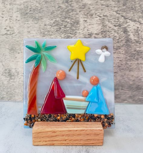 "Ethnic Fused Glass Nativity Wood Stand, Desert Holy Family Scene Decoration, Religious Gift, People of Color, Table Scape NEW this year, seems people are loving the option of desk top art.   This is a wonderful reminder of the \"meaning of the season\". This Ethnic Nativity table top decoration is full of detail.  The background glass has beautiful subtle shades of blue and rose. A lone palm tree shelters the Holy Family from the desert heat and a sweet little angel is overlooking the them in this handmade religious scene.   Measuring 4 x 4 inches and sitting in a handmade oak wood stand, this winter treat will come boxed in red and white packaging.  This adorable fused glass holiday decoration can be used displayed on a table, desk top or mantle. This would make a wonderful gift for anyo Fused Glass Nativity Scene, Christmas Fused Glass Ideas, Fused Glass Nativity, Nativity Wood, White Packaging, Fused Glass Panel, Fused Glass Christmas, Fused Glass Wall Art, Glass Art Pictures