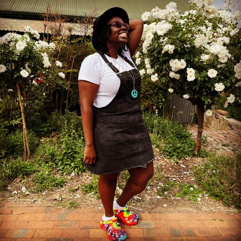 Black girl in a black dungaree denim skirt with a white shirt. For shoes she’s wearing tie dye Bae crocs clogs. She’s wearing a top hat and surrounded by roses. Bae Clog Crocs Outfit, Bae Clogs, Clogs Crocs, Colourful Things, Crocs Outfit, Tshirt Dress, Clogs, Tie Dye, Shirt Dress