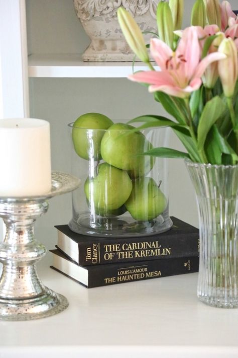 Faux green apples layered in a glass candleholder. Kitchen Bookshelf, Mantle Styling, Tall Glass Vases, Apple Decorations, Storing Craft Supplies, Green Apples, Orchid Arrangements, Velvet Pumpkins, Baby Shower Decor