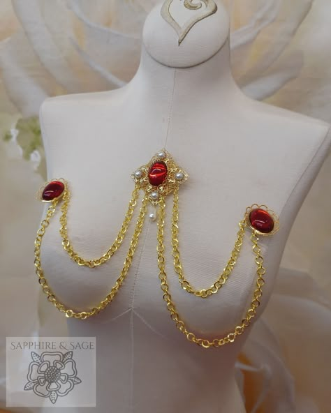 The "Wilhelmina" Swag Bodice Jewelry adds a touch of class to any period ensemble. With its Renaissance-style brooch centerpiece with swags of gold-tone chains connected to smaller brooches in matching colored stones, you'll be sure to shine. Transform your look with a timeless accessory perfect for any occasion. Red And Gold Accessories, Jewelry Corset, Ornamental Jewelry, Bra Chain, Chest Jewelry, Roman Jewelry, Cosplay Jewelry, Light Sapphire, Greek Jewelry