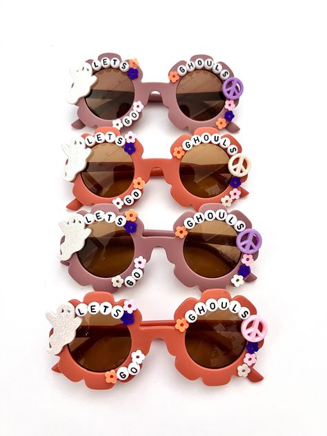 "\"LETS GO GHOULS\" adorable HALLOWEEN SUNNIES!! Each pair is handcrafted by me. Using various beads, Charms, Rhinestones, and fun details. On our adorable boho flower sunnies!! Choose between our gorgeous PLUM OR RUST color. * Anti-Glare * UV Protection (UVA & UVB) * Durable and shatterproof  * They open and close smoothly  * Each item is made to order and will be ready to ship in 5-7 business days! If you need your order sooner. Please check out my \"RUSH ORDER OPTION\".  https://www.etsy.com/EyeCandyandFluff/listing/1286351273/rush-my-order-please *SHOP DISCLAIMER/WAIVER!  * Do NOT let your child put the sunglasses in their mouth as beads can become detached.    Always monitor and supervise while children are wearing these. The shop assumes no responsibility for sunglasses made. Sizing- Halloween Sunglasses Diy, Trendy Halloween Festival Sunglasses, Fun Orange Plastic Sunglasses, Playful Orange Plastic Sunglasses, Fun Festival Sunglasses With Gradient Lenses, Fun Handmade Pink Sunglasses, Festival Fun Sunglasses With Gradient Lenses, Fun Festival Sunglasses With Tinted Lenses, Handmade Fun Pink Sunglasses