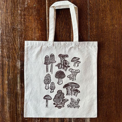 reminder that I recently added these block printed mushroom totes to my shop! I realized that I posted a “coming soon” reel when I made them but never really announced that they’re available 😅 so here they are! | #mushrooms #mushroomart #mushroomdecor #totebag #foraging #blockprinting #printmaking #linocut #printmaker #reliefprinting #blockprint #speedballart #mushies Linocut Tote Bag, Lino Print Tote Bag, Block Print Tote Bag, Sgraffito Ideas, Different Types Of Mushrooms, Printmaking Linocut, Types Of Mushrooms, Nature Motifs, Lino Art