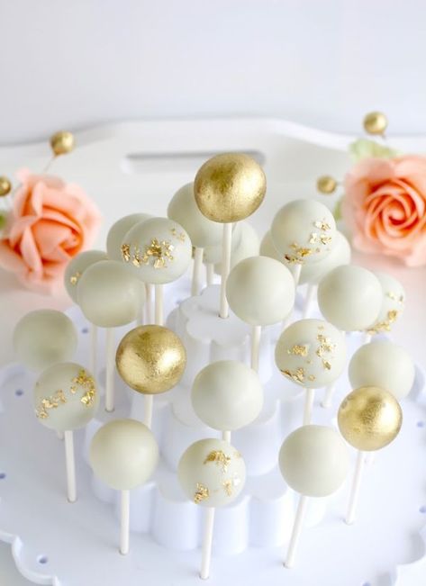 Wedding cake pops decorated in white and gold with pink flowers in the background Cake Pops For Engagement Party, Cake Pops Engagement, Wedding Cake Pops Ideas, White And Gold Cake Pops, Cake Pop Centerpiece, Engagement Party Desserts, Cake Pops Ideas, Gold Cake Pops, Incentive Ideas